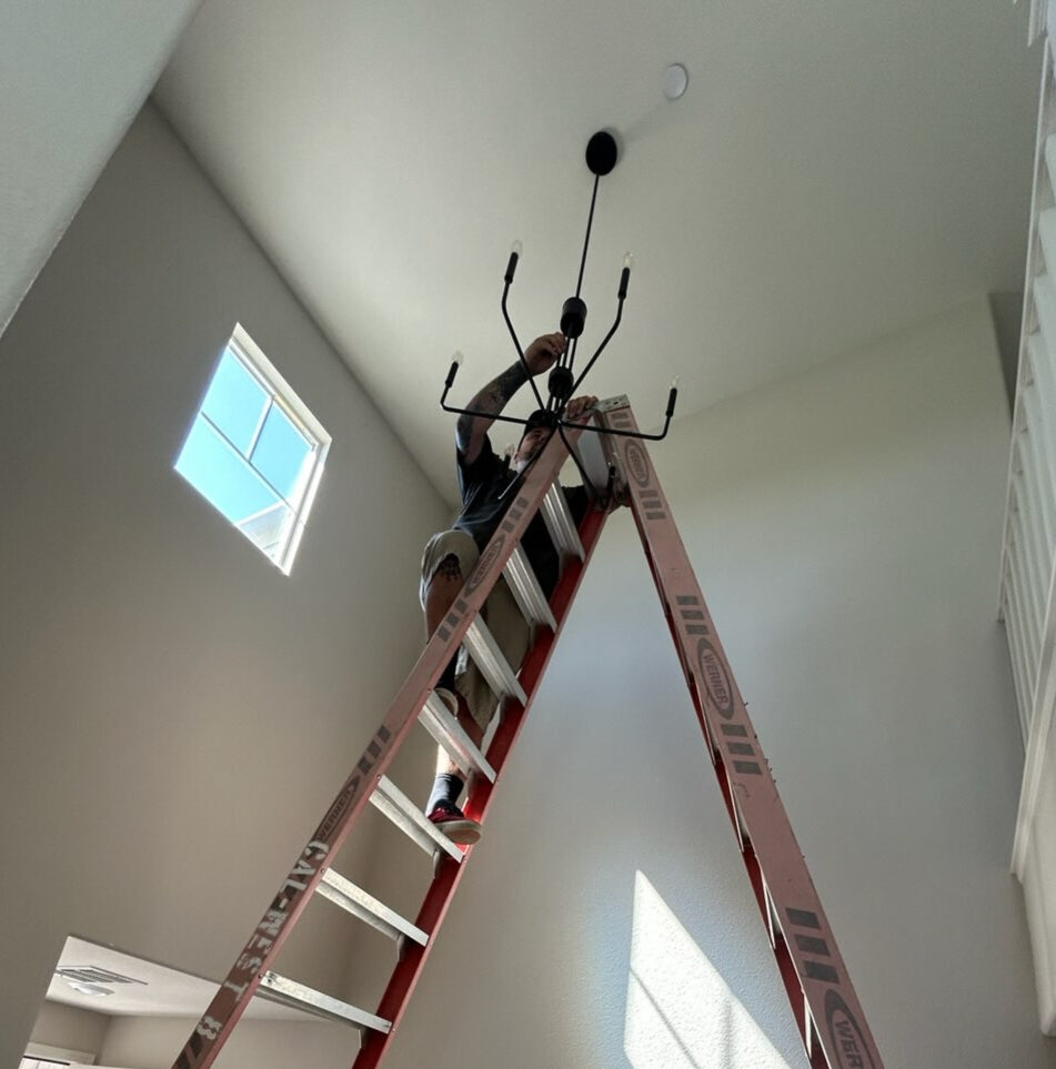 All Covered Electric installing a chandelier from a ladder in a vaulted entry