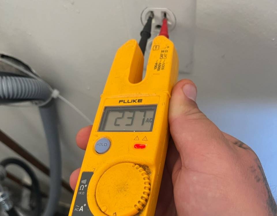 Electrician verifying line voltage at an outlet with a Fluke meter