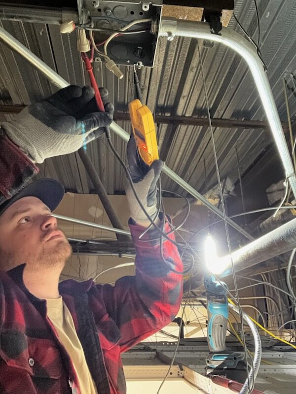 All Covered Electric technician metering a circuit in an open ceiling